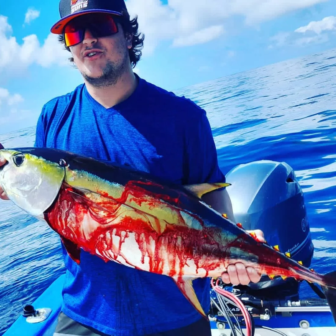 An angler holding a yellowfin tuna aboard, open ocean behind